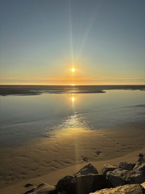 A desert landscape with a clear sky and the sun low on the horizon, casting a reflection on the water. - 2-bedroom condo in tranquil North Wildwood with AC (North Wildwood)