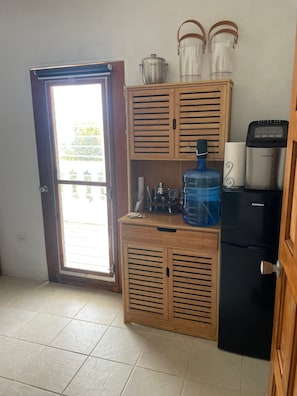 Una cocina compacta con refrigerador integrado, dispensador de agua y cafetera.