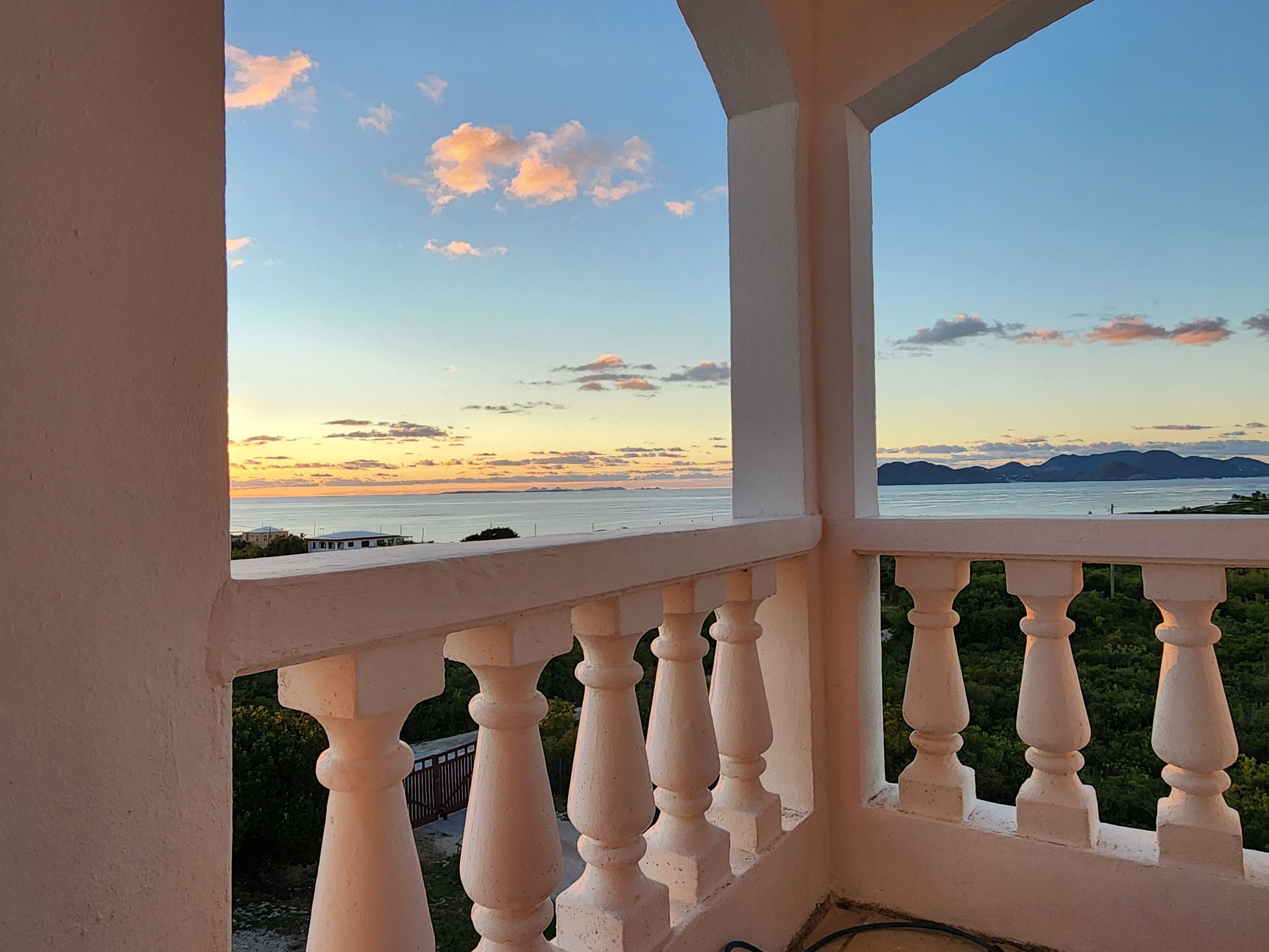Un balcón con vistas a una puesta de sol sobre un cuerpo de agua y montañas lejanas.