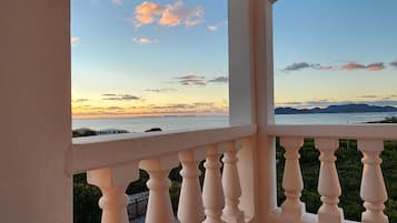 Un balcón con vistas a una puesta de sol sobre un cuerpo de agua y montañas lejanas.