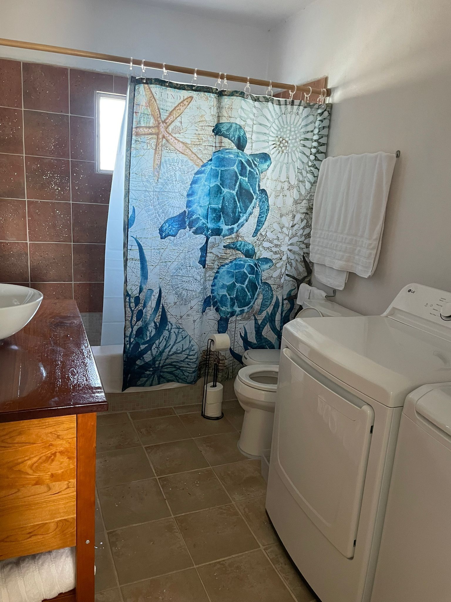 Un baño con un mural de tortuga marina, un tocador de madera, un inodoro y una lavadora.