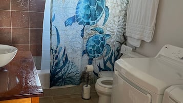 Un baño con un mural de tortuga marina, un tocador de madera, un inodoro y una lavadora.