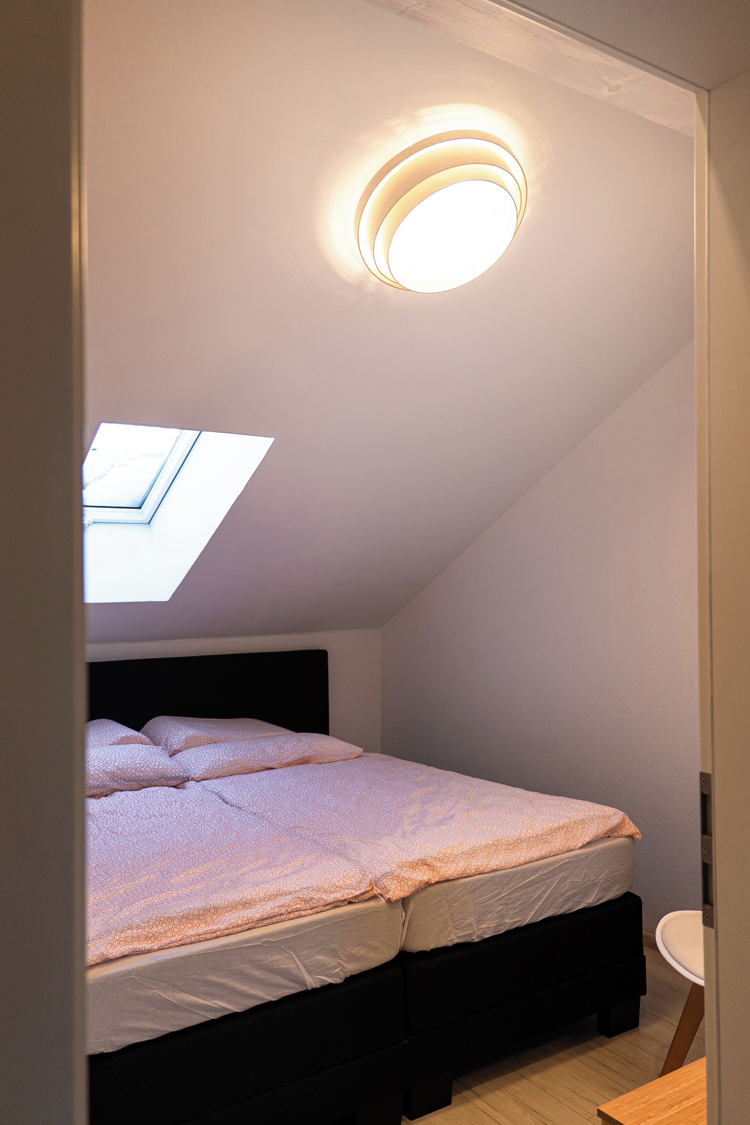 A bedroom with a skylight, a bed with a headboard, and a bedside table.