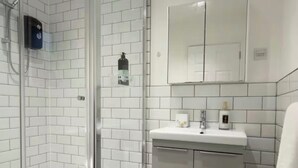 A modern bathroom with a glass-enclosed shower, white tiled walls, a white sink with a mirror above, and a small rug on the floor. - Premium Luxe Collection (Leicester)
