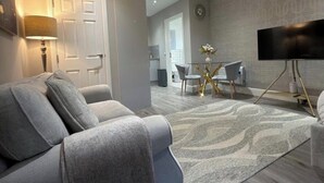 A modern living room with a grey sofa, a coffee table, and a flat-screen TV. - Premium Luxe Collection (Leicester)