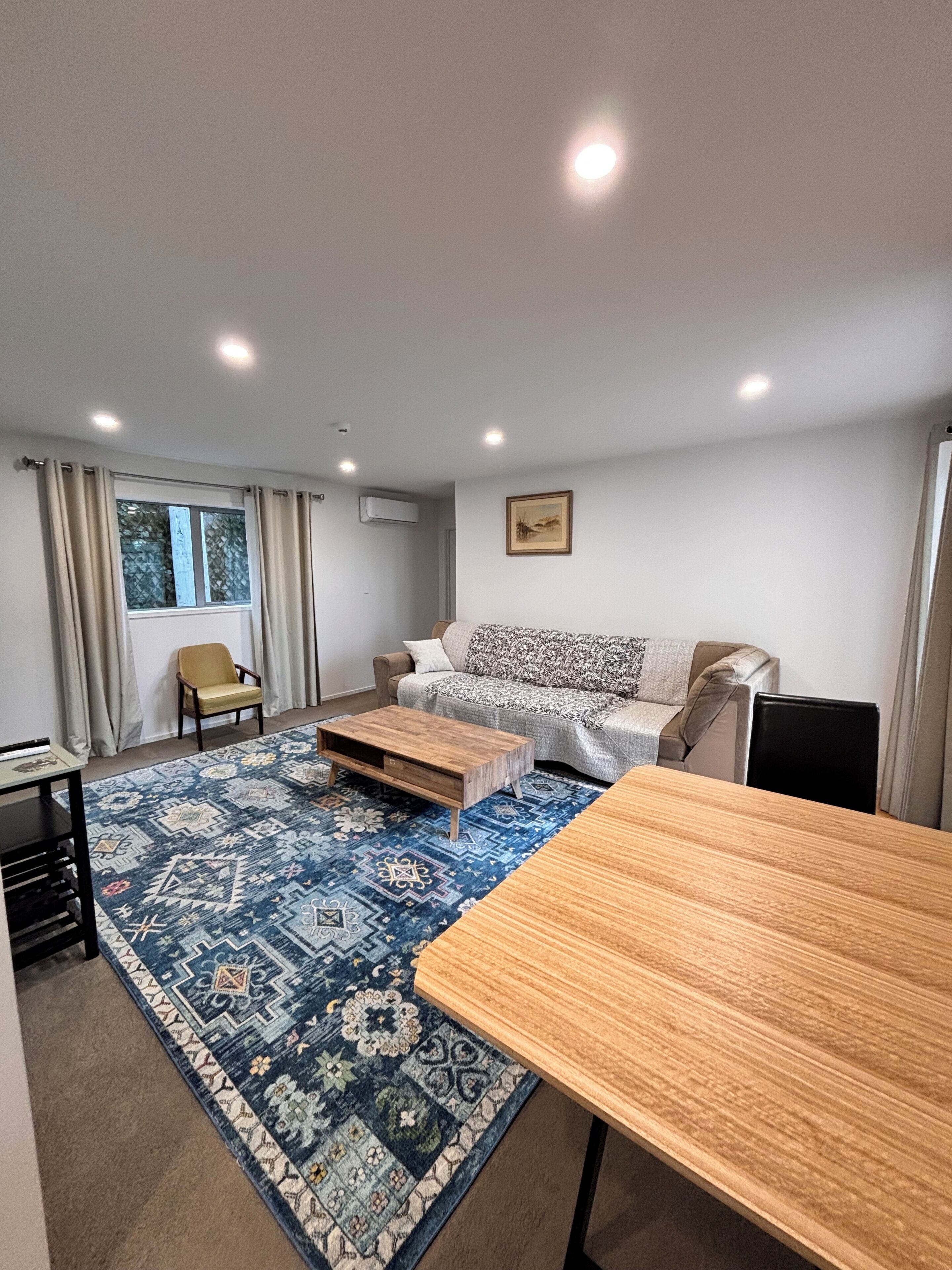 A modern living room with a sofa, a coffee table, a dining table, and a patterned rug.