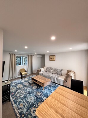 A living room with a sofa, a coffee table, a chair, a TV, and a patterned rug. - private, secured, close to the beach shops cafe (Auckland)