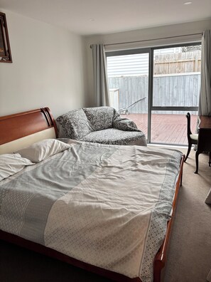 Een slaapkamer met een groot bed, een bank, een bureau en uitzicht op een houten schutting door een schuifdeur.'