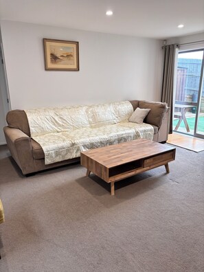 A living room with a beige sofa, a wooden coffee table, and a painting on the wall. - private, secured, close to the beach shops cafe (Auckland)