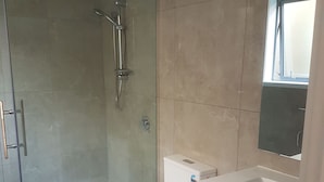Un baño moderno con ducha de vidrio, inodoro blanco y lavamanos con espejo.