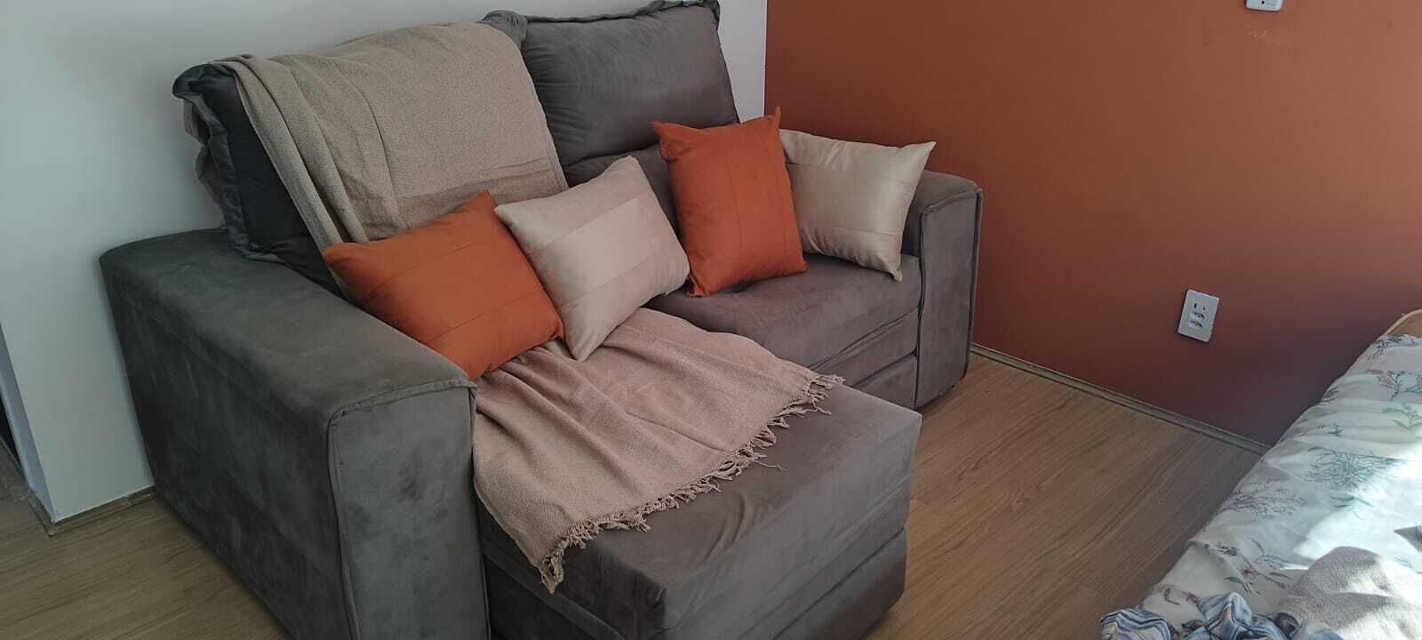 A grey sofa with a beige throw blanket and three cushions in orange, beige, and grey.