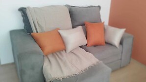 A grey sofa with a beige throw blanket and three cushions in shades of grey, orange, and white. - Apartment in the Rio Wonder Condominium - Downtown Rio de Janeiro. Close to EVERYTHING. (Rio de Janeiro)
