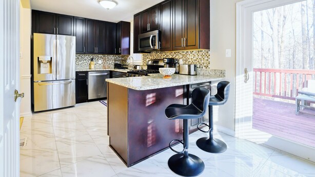 A modern kitchen with dark cabinets, stainless steel appliances, a marble countertop, and a bar stool area. - Wooded 3BR Retreat Near DC: Free Parking. Pet/Infant/Kids-Friendly. Private Deck (Silver Spring)