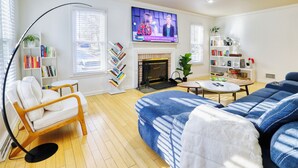 A living room with a sofa, a chair, a fireplace, a TV, and bookshelves. - Wooded 3BR Retreat Near DC: Free Parking. Pet/Infant/Kids-Friendly. Private Deck (Silver Spring)