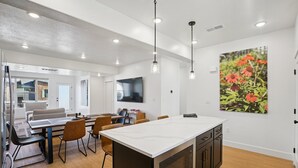 A modern kitchen with a central island, dining area with chairs, and a large window. - Risen Ranch by Crafty Casitas Hospitality (Mountain Green)