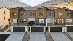 A modern multi-story residential building with a garage, a covered outdoor seating area, and a mountain backdrop. - Risen Ranch by Crafty Casitas Hospitality (Mountain Green)