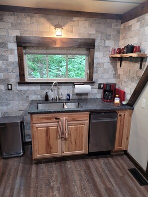 A kitchen with a stone wall, wooden cabinets, a built-in sink, a window, and a coffee machine.