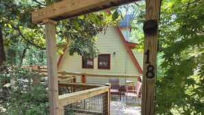 A wooden deck leading to a house with a number 18 sign, surrounded by greenery.
