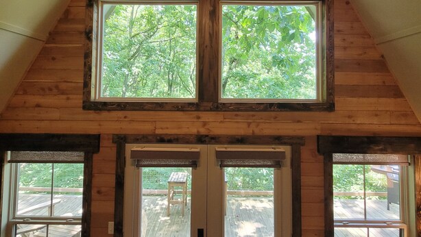 A wooden attic room with a sloped ceiling, two windows, and a door leading to an outdoor deck.