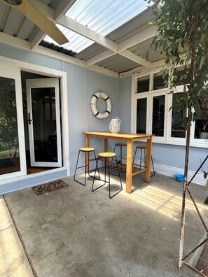 A covered patio with a table and stools, a door, and a window. - Florence by the beach: cosy family home in a quiet street yet central (Capel Sound)