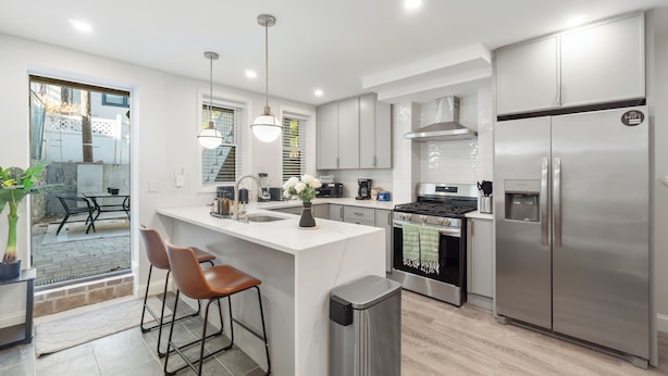 A modern kitchen with a central island, stainless steel appliances, and a view to an outdoor patio. - Ground Level 1BR/2BATH w 2Queens apartment, near PATH station w + W/D (Jersey City)