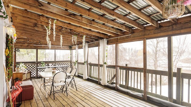 A covered outdoor deck with wooden flooring, a table with chairs, and a railing. - Cozy Pet-Friendly Waterfront Chalet (Mercier)