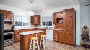 A modern kitchen with wooden cabinets, a central island with stools, a built-in oven, and a dishwasher. - Cozy Pet-Friendly Waterfront Chalet (Mercier)