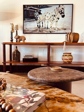 A living room with a round stone table, wooden shelves, and a painting of horses. - Villa Amani. Beachfront house in Ferradura. Comfort, Elegance, Privacy. (Armação dos Búzios)