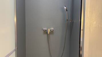 Un petit espace douche fermé, avec un mur gris, une pomme de douche et un pommeau de douche amovible.