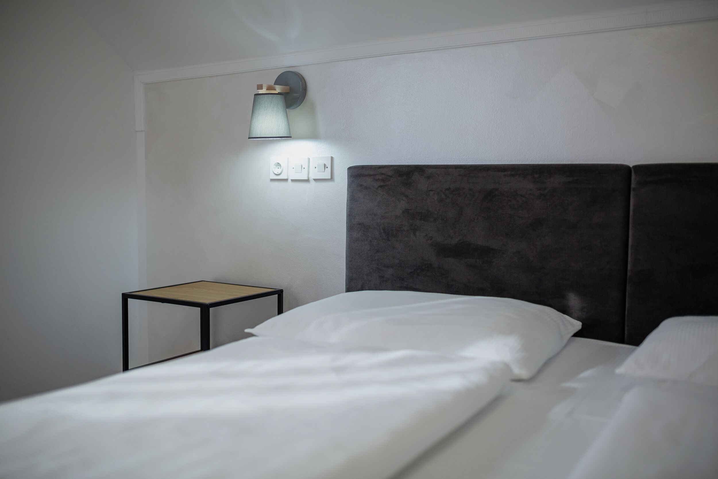 Habitación de hotel con cama, mesita de noche, luz de pared y toma de corriente.
