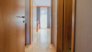 Un pasillo con puertas de madera, suelo de baldosas y vistas a una habitación con una silla y cortinas.