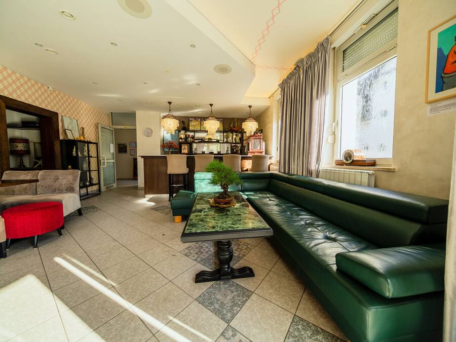 A living room with a green sofa, a red chair, a coffee table with a plant, and a kitchen area in the background.
