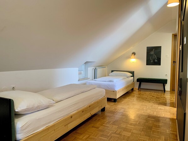 Una habitación con dos camas de madera, un banco, una lámpara en la pared y un radiador.