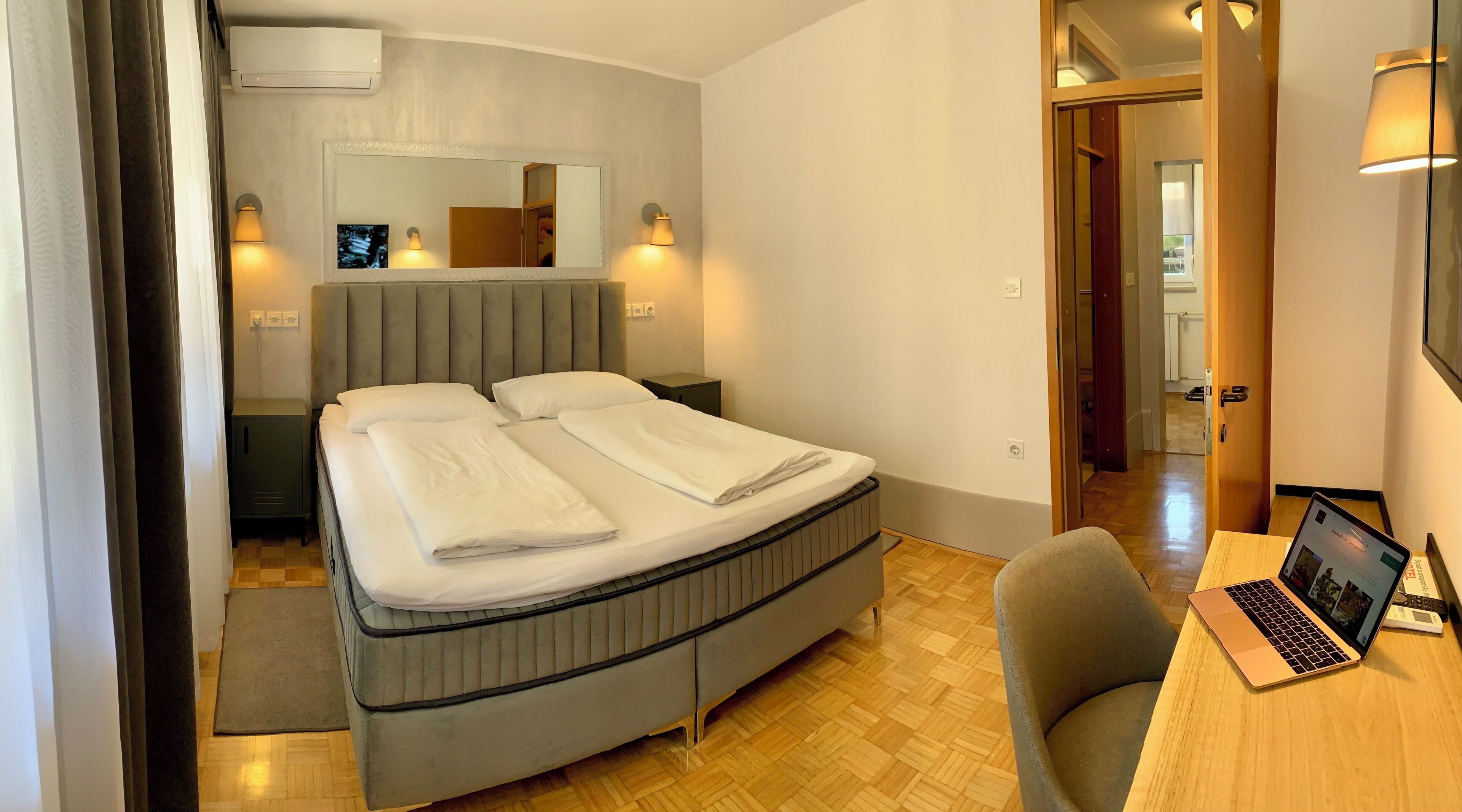 A hotel room with a bed, bedside lamps, a desk with a laptop, and a mirror.