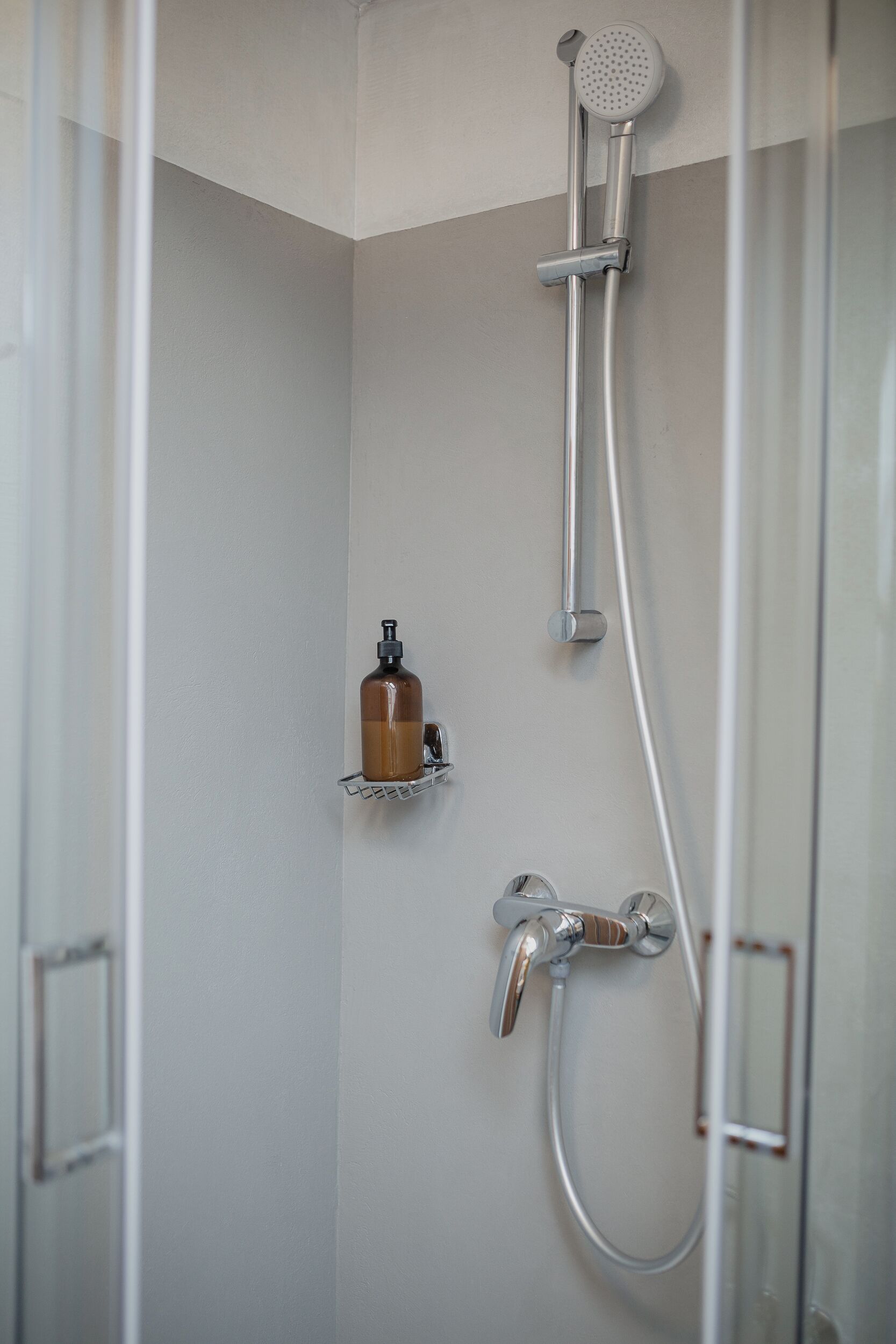 Dusche mit Duschbrause, Handfasser und Seifenspender auf einer Wandablage.