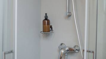 A shower with a handheld showerhead, a handheld faucet, and a soap dispenser on a wall-mounted shelf.
