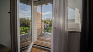 A balcony with a wooden deck, a metal railing, and a view of a green landscape.