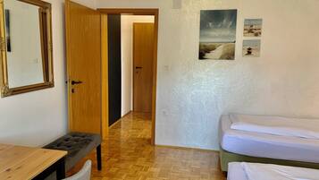 Ein Zimmer mit Holzboden, einem Schreibtisch mit Stuhl, einem Bett, einer Tür und einer Wand mit Bildern.