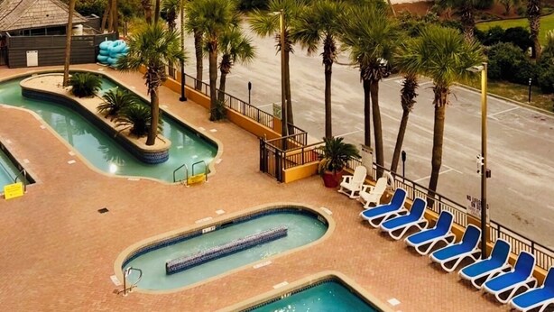 A pool area with multiple swimming pools, palm trees, and a beach view. - Charming studio in soothing Myrtle Beach with fitness room, multiple pools (Myrtle Beach)