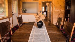 A wooden dining room with a long table, chairs, and a vase of dried flowers. - The Carriage House / Walk to River & Lake, In Town (Grand Lake)