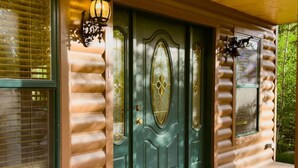 A log cabin with a green door, two windows with blinds, and a porch with a patterned rug. - The Carriage House / Walk to River & Lake, In Town (Grand Lake)
