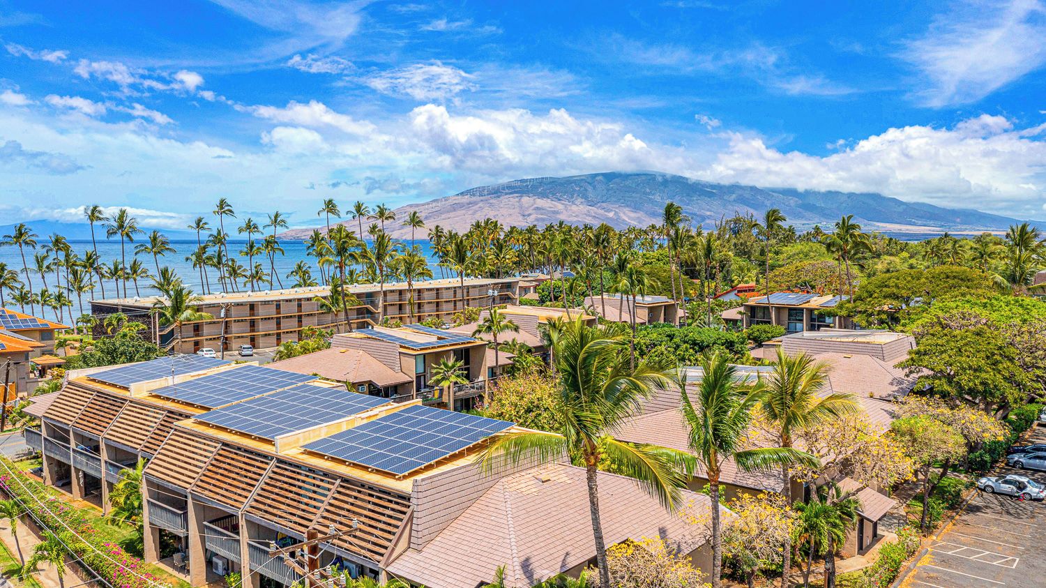 A resort with multiple buildings, solar panels on roofs, and a view of the ocean and mountains.