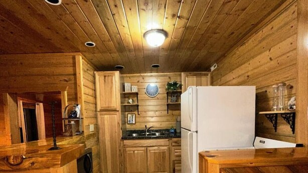 A wooden cabin interior with a kitchen area, including wooden cabinets, a refrigerator, and a sink. - The Red Bears Den / Walk to River & Lake, In Town (Grand Lake)