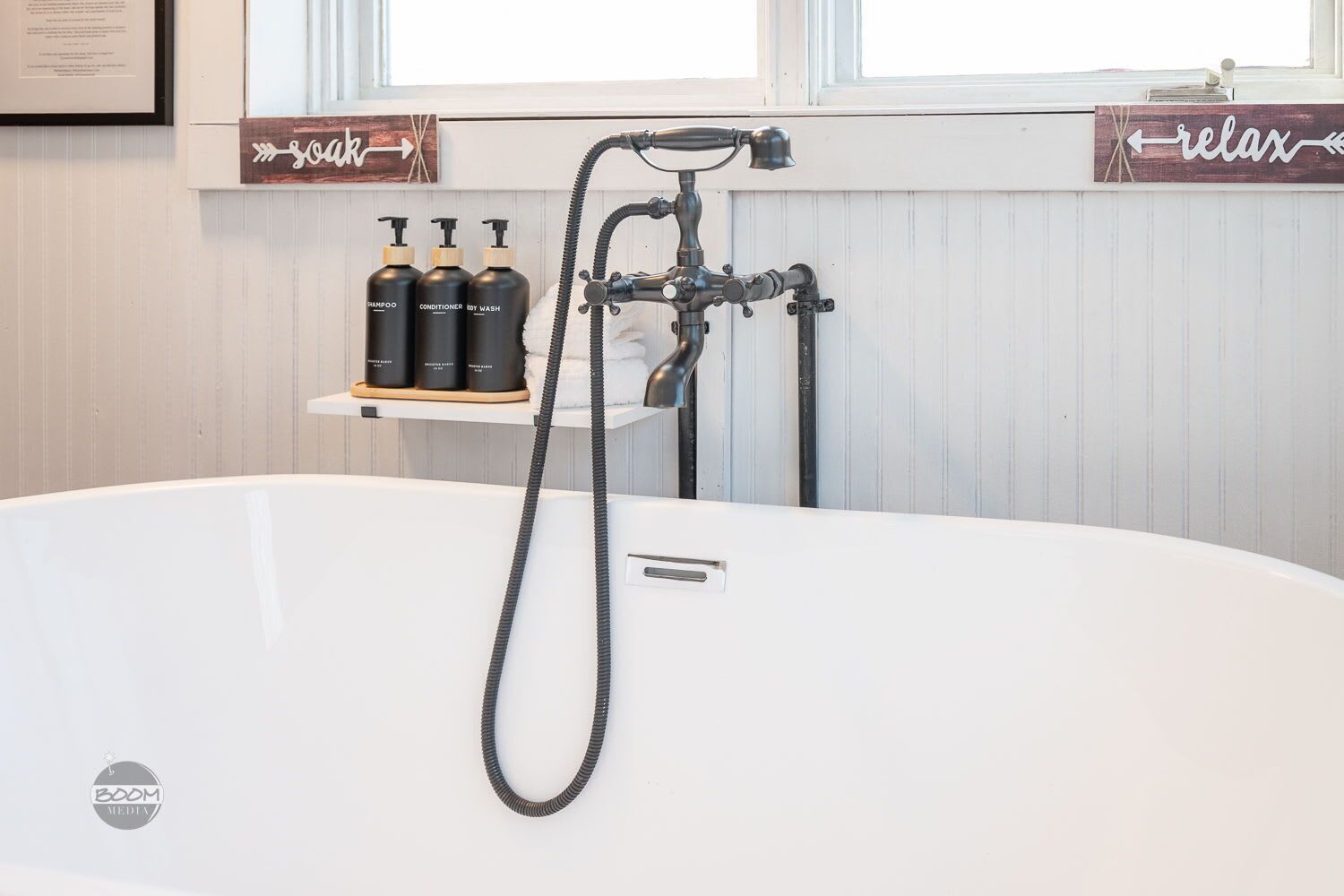 Ein Badezimmer mit einer weißen Badewanne, einer Duschbrause und drei Flaschen Shampoo, Conditioner und Duschgel auf einem Regal.
