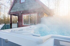 Un bain à remous devant une cabane en bois dotée d’une porte en verre.