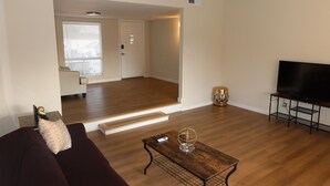 Ein Wohnzimmer mit Sofa, Couchtisch, TV-Schrank und einer Treppe zu einem anderen Raum.