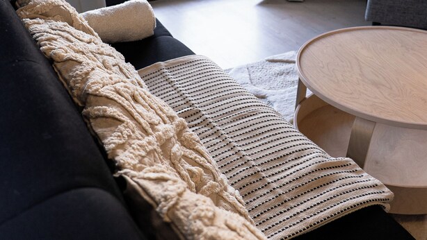 Una sala de estar moderna con un sofá negro, una manta color beige y una mesa de centro de madera.