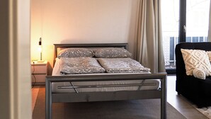 Un dormitorio con cama, mesita de noche y ventana con cortinas.