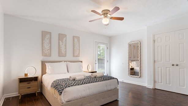 Une chambre à coucher avec un lit, des tables de chevet, un ventilateur de plafond et une porte.