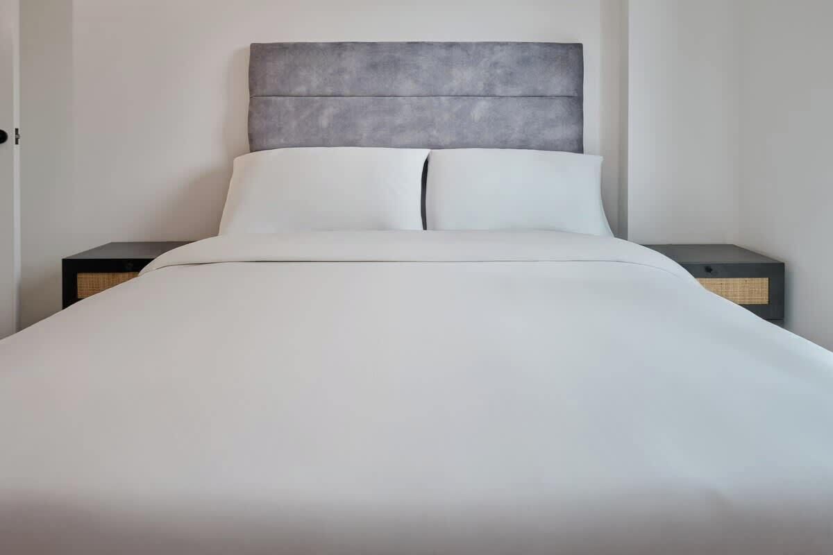 A bed with a grey headboard, white bedding, and two bedside tables.
